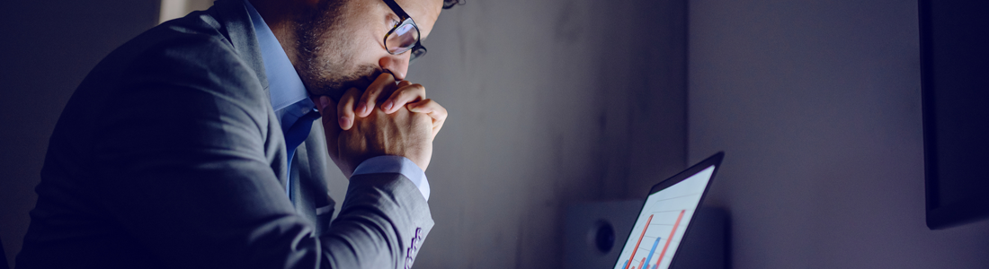 Businessman in suit leaning on desk and looking at charts.